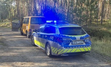 na załączonym zdjęciu  numer 1 i numer 2 widoczny jest radiowóz oznakowany, z włączoną sygnalizacją świetlną, i bus marki volkswagen T4, koloru żółtego, w tle widoczne są drzewa, las.